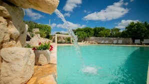 A clear blue pool with a stone wall and a water feature. - Trulli Arco Antico (Locorotondo)