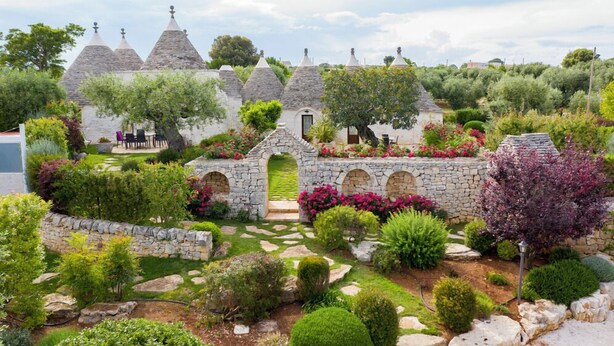 A garden with stone structures, a central archway, and various plants. - Trulli Arco Antico (Locorotondo)