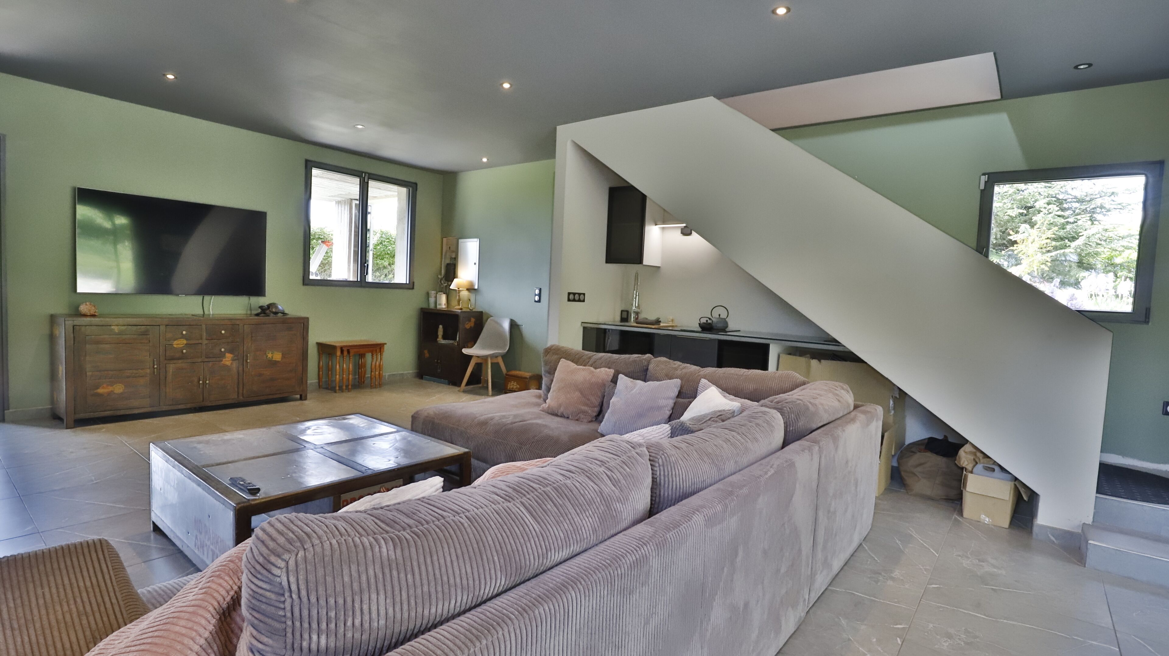 A modern living room with a large sectional sofa, a flat-screen TV, and a staircase leading to an upper level.