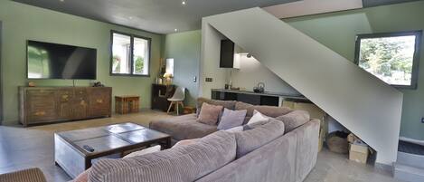 A modern living room with a large sectional sofa, a flat-screen TV, and a staircase leading to an upper level.