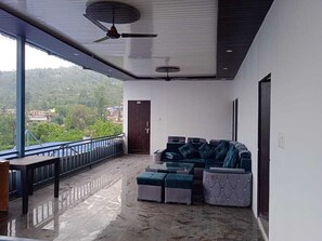A balcony with a seating area, a ceiling fan, and a view of the surrounding landscape. - Sri Ram Resorts & Restaurant (Ukhimath)