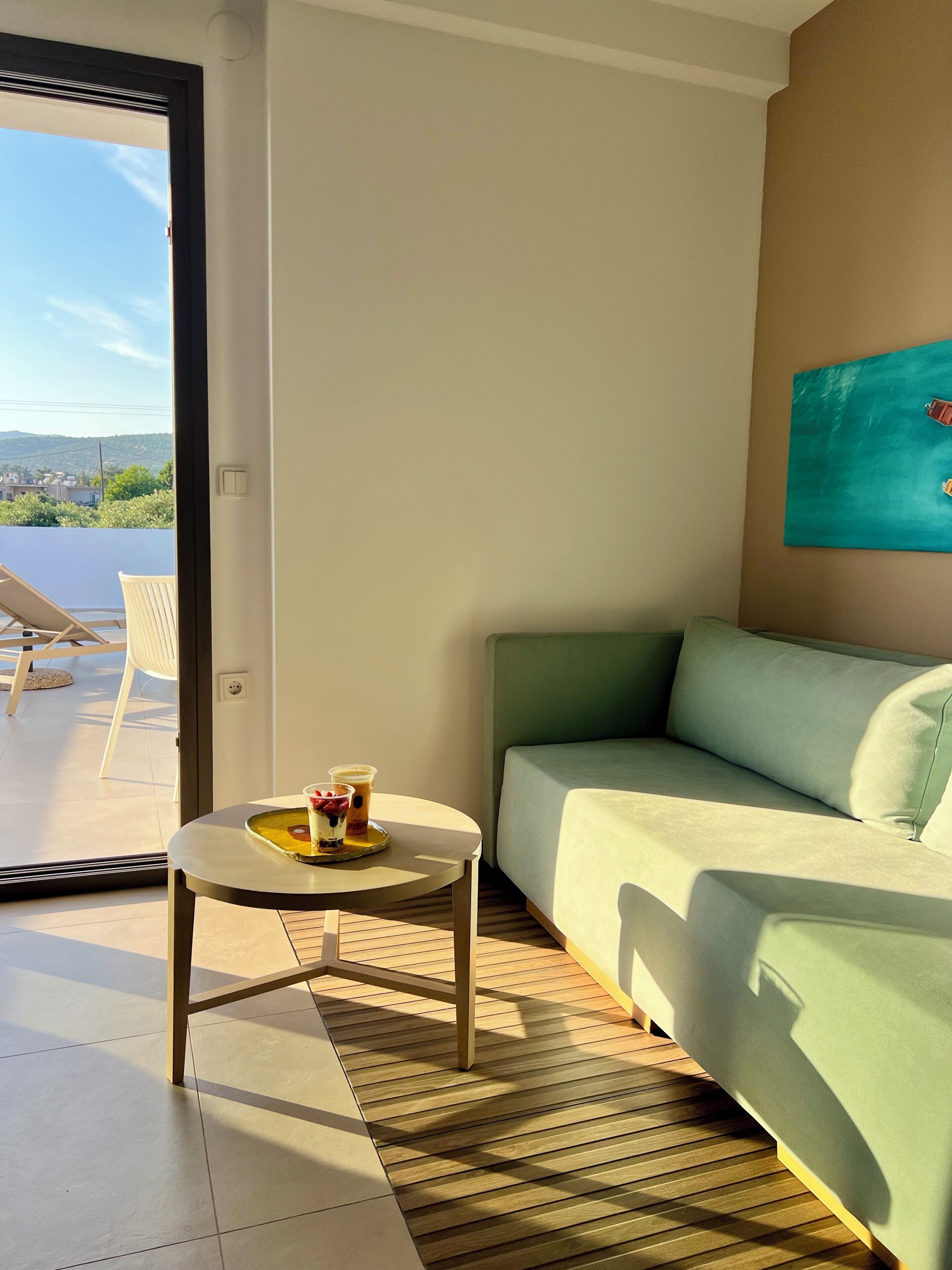 Un salón moderno con un sofá verde, una mesita redonda con bebidas y vistas al exterior.