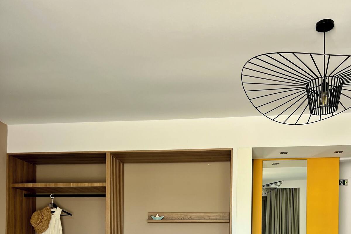 A hotel room with a bed, a seating area with a chair and table, a wardrobe, and a mirror.