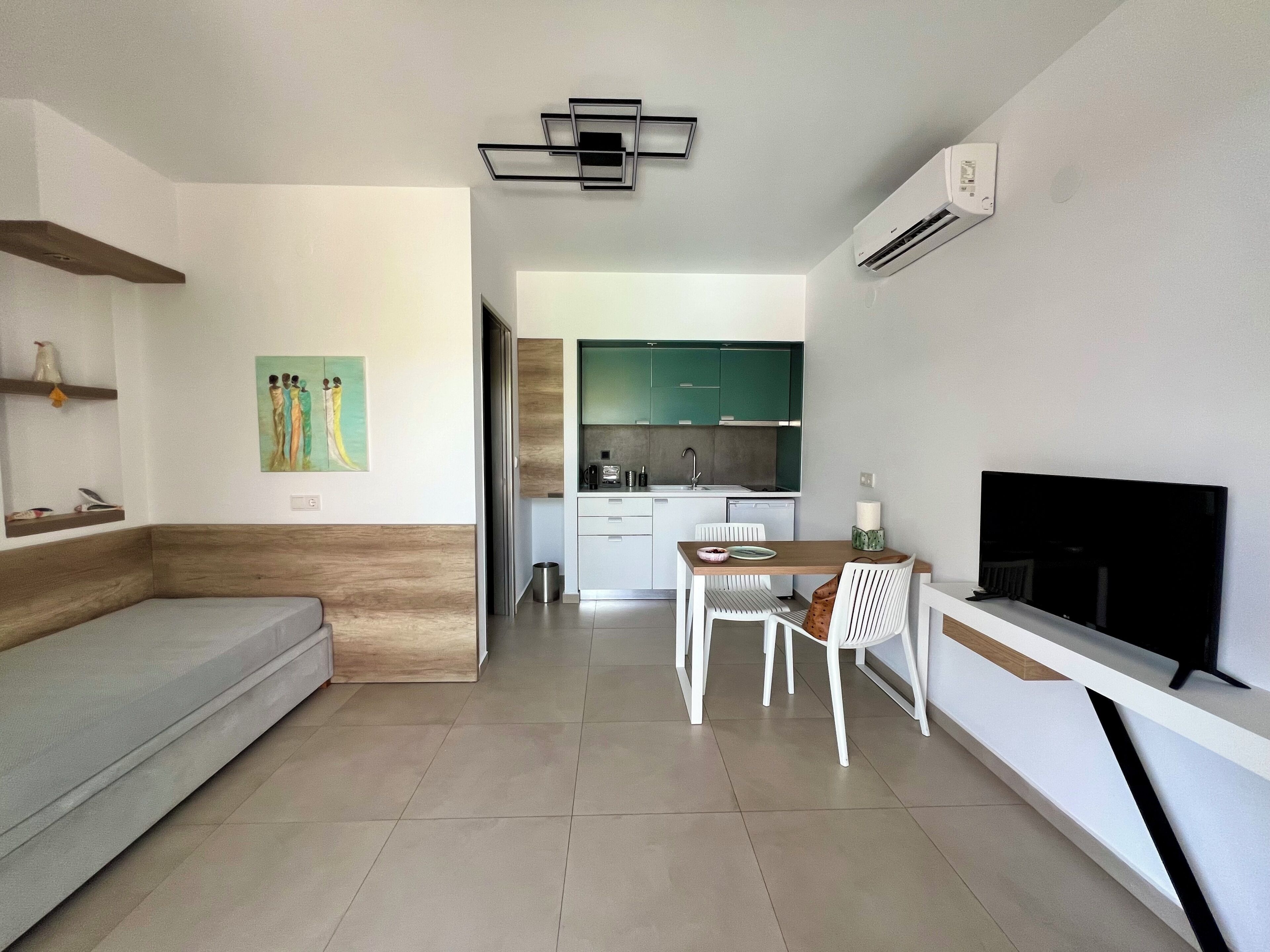 A modern living room with a sofa, a dining table with chairs, a flat-screen TV, and a kitchen area in the background.