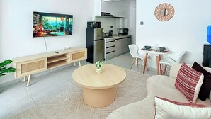 Ett modernt vardagsrum med en tv, soffa, soffbord och ett kök synligt i bakgrunden.