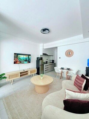 A modern living room with a TV, sofa, coffee table, and kitchen in the background. - Cozy 1-bedroom apartment in fantastic Nairobi Westlands with AC and gym access (Nairobi)
