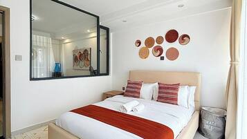A modern hotel room with a large bed, a mirror, wall decor, and a storage bin.