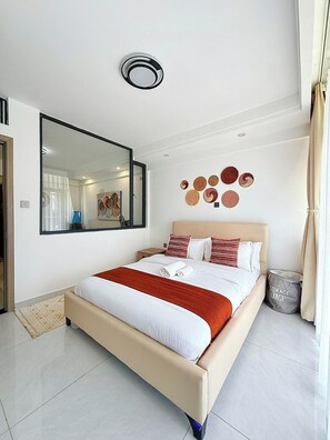 A modern hotel room with a large bed, a mirror, wall decor, and a storage bin. - Cozy 1-bedroom apartment in fantastic Nairobi Westlands with AC and gym access (Nairobi)
