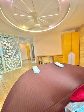 Een moderne hotelkamer met een groot bed, een houten garderobe, een bureau en een decoratief plafond.