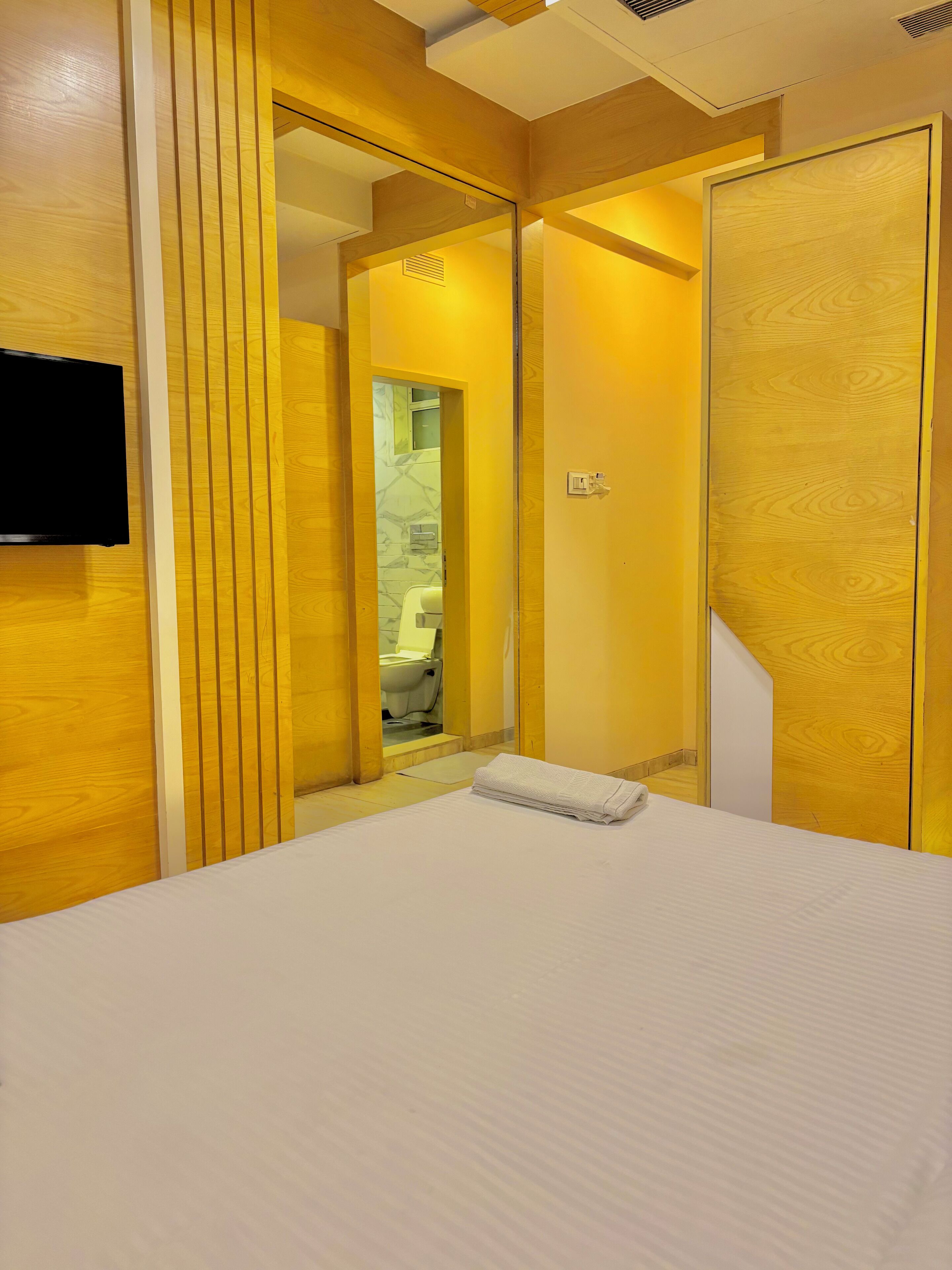 Een hotelkamer met een bed, een aan de muur bevestigde televisie en een zichtbare badkamer achter een glazen deur.