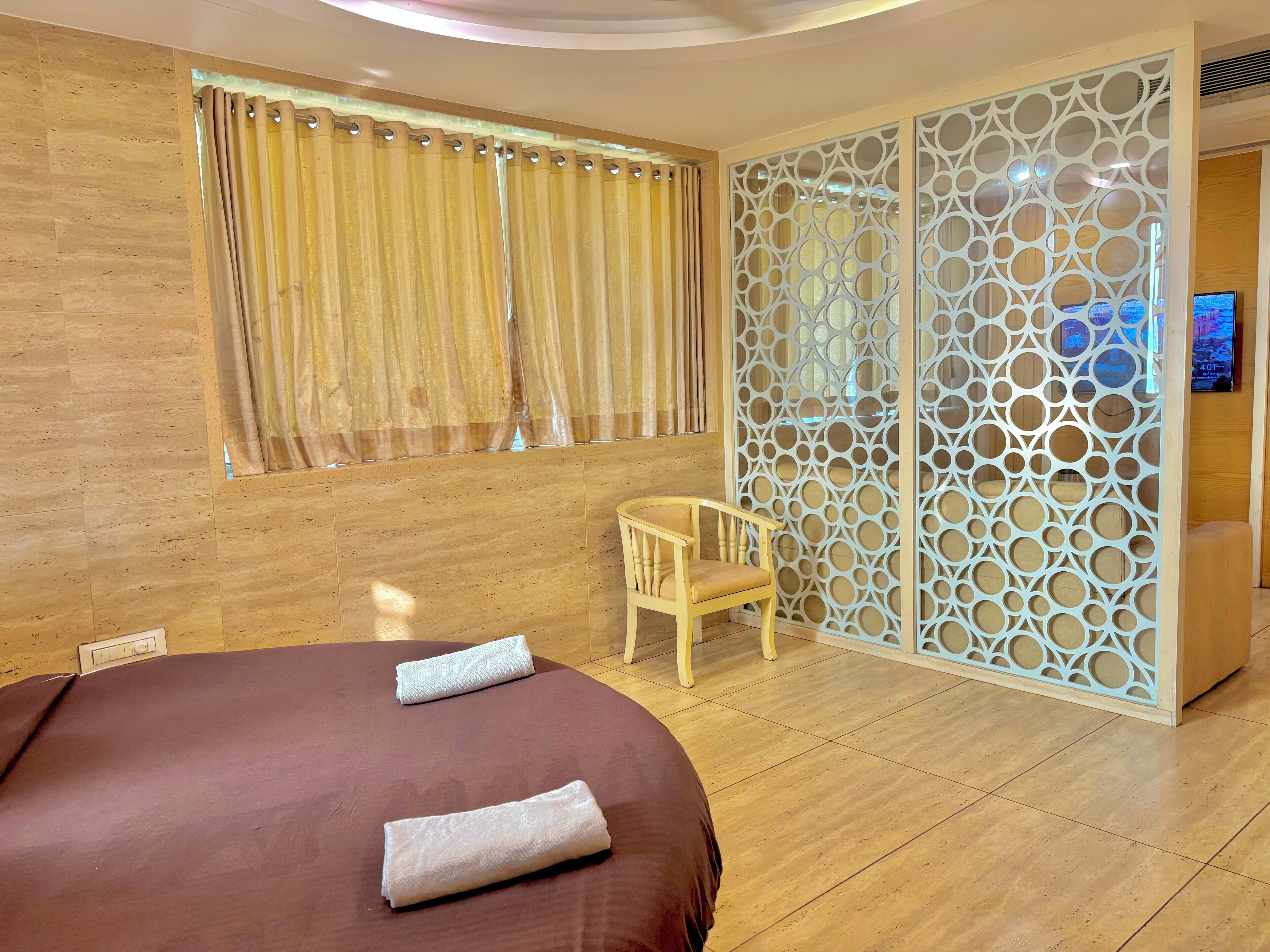 Una habitación de hotel con cama, una silla, un separador decorativo y un televisor.