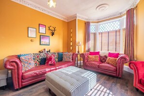 A living room with two red leather sofas, a striped ottoman, and a small table with a lamp.