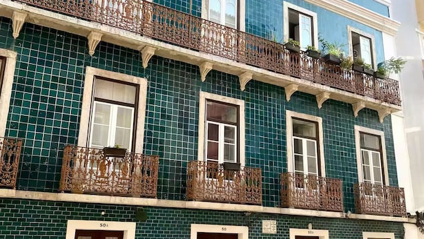 Un immeuble à plusieurs étages, doté d’une façade recouverte de carreaux bleus, de balcons décoratifs et de portes numérotées.
