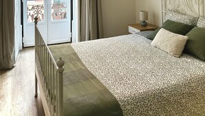 Une chambre à coucher avec un lit, une table de chevet, une lampe, un luminaire suspendu, une vue à travers une porte et un balcon.