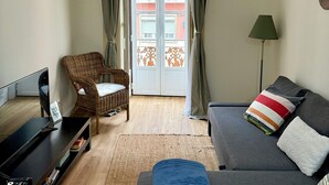 Un salon comprenant un canapé, un téléviseur, un fauteuil en osier et une vue sur l’extérieur par une fenêtre ornée de rideaux.