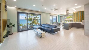 A spacious living area with a sofa, a dining table, and a view of the sea. - Sacheon Bireong Pool Villa (Sacheon)