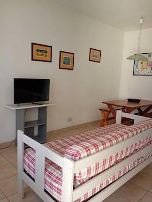 A small room with a bed, a TV on a stand, a table, and three framed pictures on the wall.