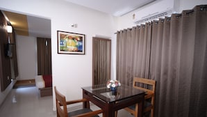 A dining area with a glass table, wooden chairs, a vase with flowers, and a painting on the wall. - HOTEL DE GRAND MALABAR (Kozhikode)