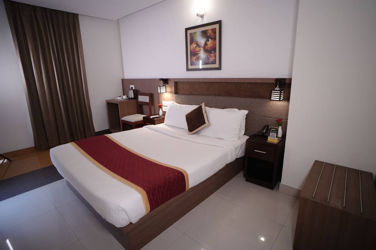 A hotel room with a large bed, a nightstand, a desk, a chair, a lamp, and a painting on the wall.