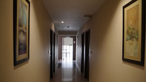 A long, narrow hallway with framed artwork on the walls, recessed lighting, and a reflective floor. - HOTEL DE GRAND MALABAR (Kozhikode)