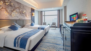 Ein Hotelzimmer mit zwei Betten, einem Fernseher, einem Schreibtisch und Blick auf die Stadt.