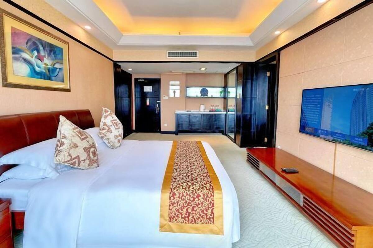 Habitación de hotel con cama, televisión, escritorio y baño visible a través de una puerta abierta.