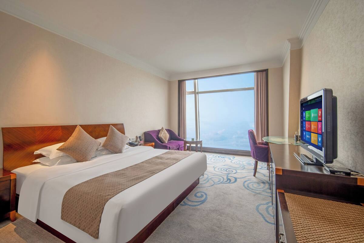 Habitación de hotel con una cama grande, un televisor, un escritorio y vistas al cielo.