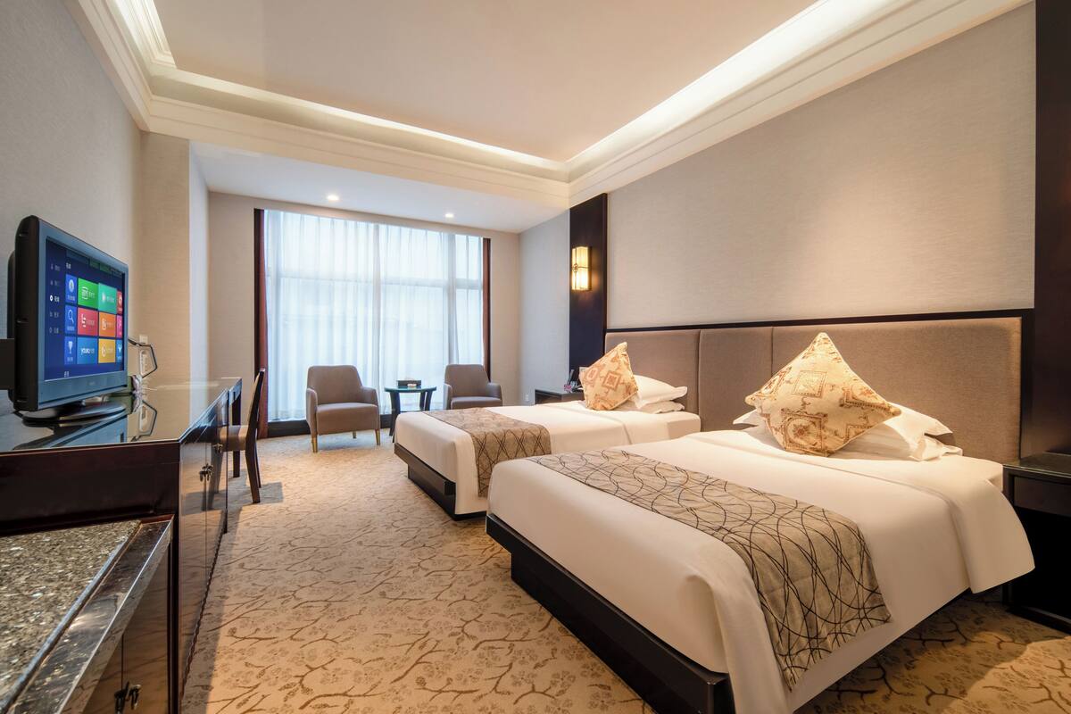 Habitación de hotel con dos camas, televisión, escritorio, silla y ventana grande.