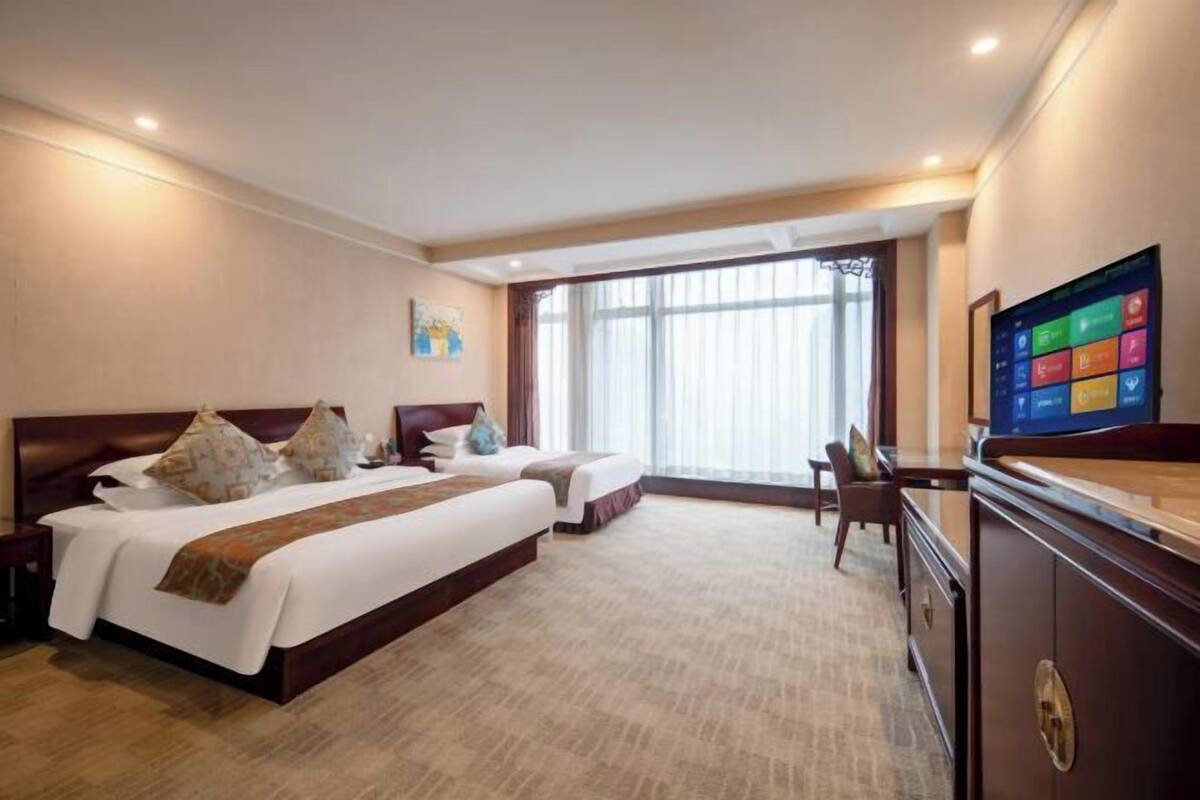 Habitación de hotel con dos camas, televisión, escritorio y un amplio ventanal.