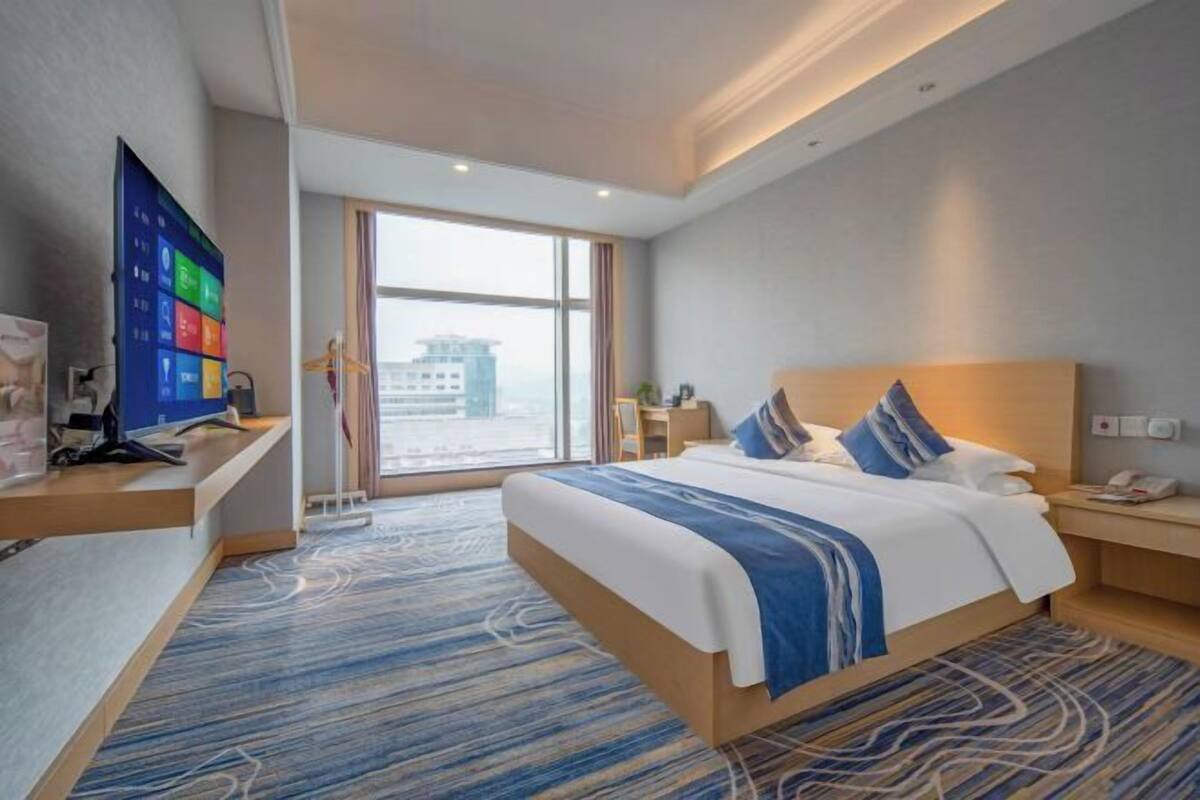 Habitación de hotel con una cama grande, un escritorio, televisión y vistas a la ciudad.