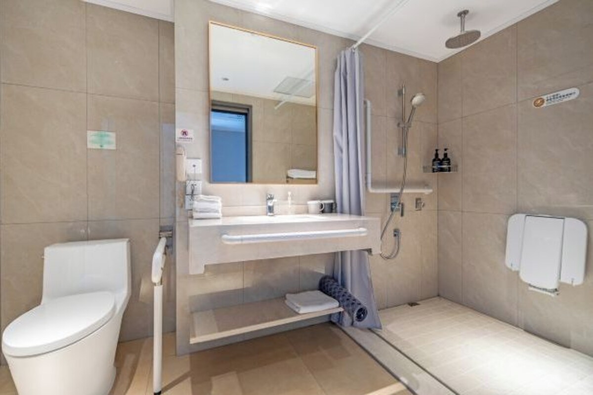 Un baño moderno con inodoro, lavamanos, espejo, ducha y toallero.