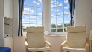 A room with two beige chairs, a white table, and a window with curtains.