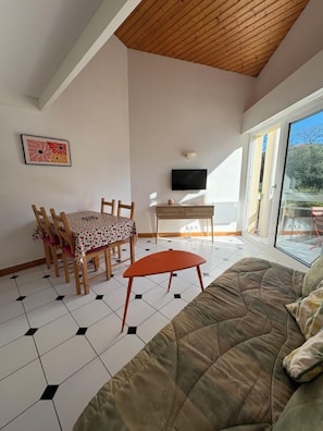 Ein Zimmer mit Esstisch, Stühlen, einer Couch, einem Fernseher und einem großen Fenster.