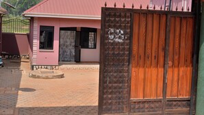 Un bâtiment rose avec une entrée fermée par un portail, une clôture en métal et une allée pavée.