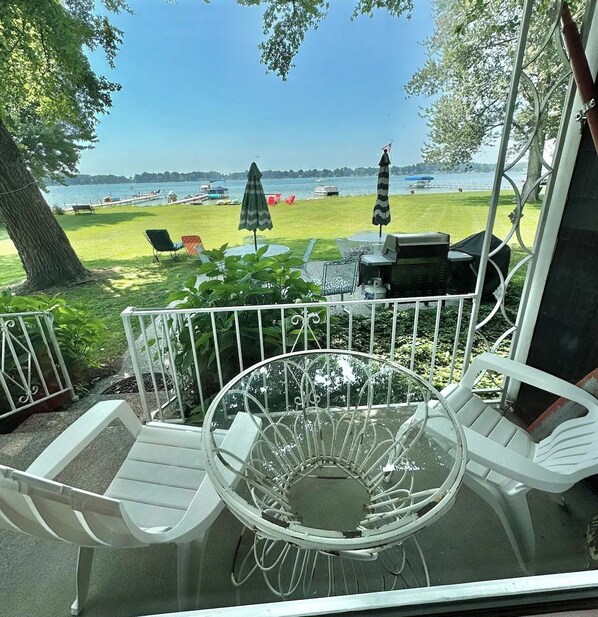 A patio with a table and chairs, overlooking a lake with boats and a grassy area.