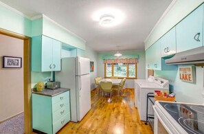 A compact kitchen with teal cabinets, a refrigerator, a washing machine, and a dining area with a table and chairs.