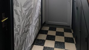 Een smalle gang met een geruit vloerkleed, een deur met raam en een wand met een botanisch behangpatroon.