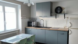 Een moderne keuken met een eethoek, met een witte radiator, een magnetron, een spoelbak en een bordje met de tekst 'koffie' aan de muur.