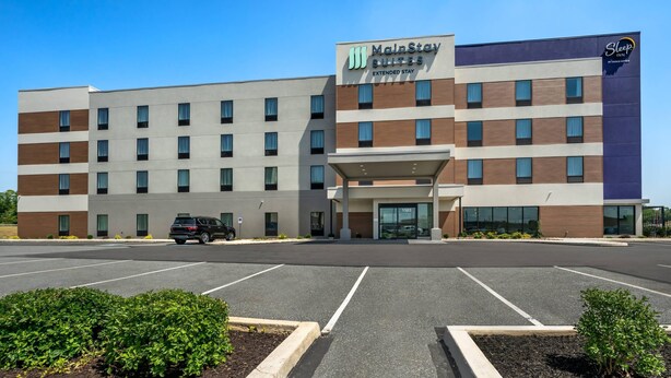 A MainStay Suites Extended Stay hotel with a parking lot and a black SUV parked in front. - MainStay Suites Harrisburg Airport - Hershey South (Middletown)