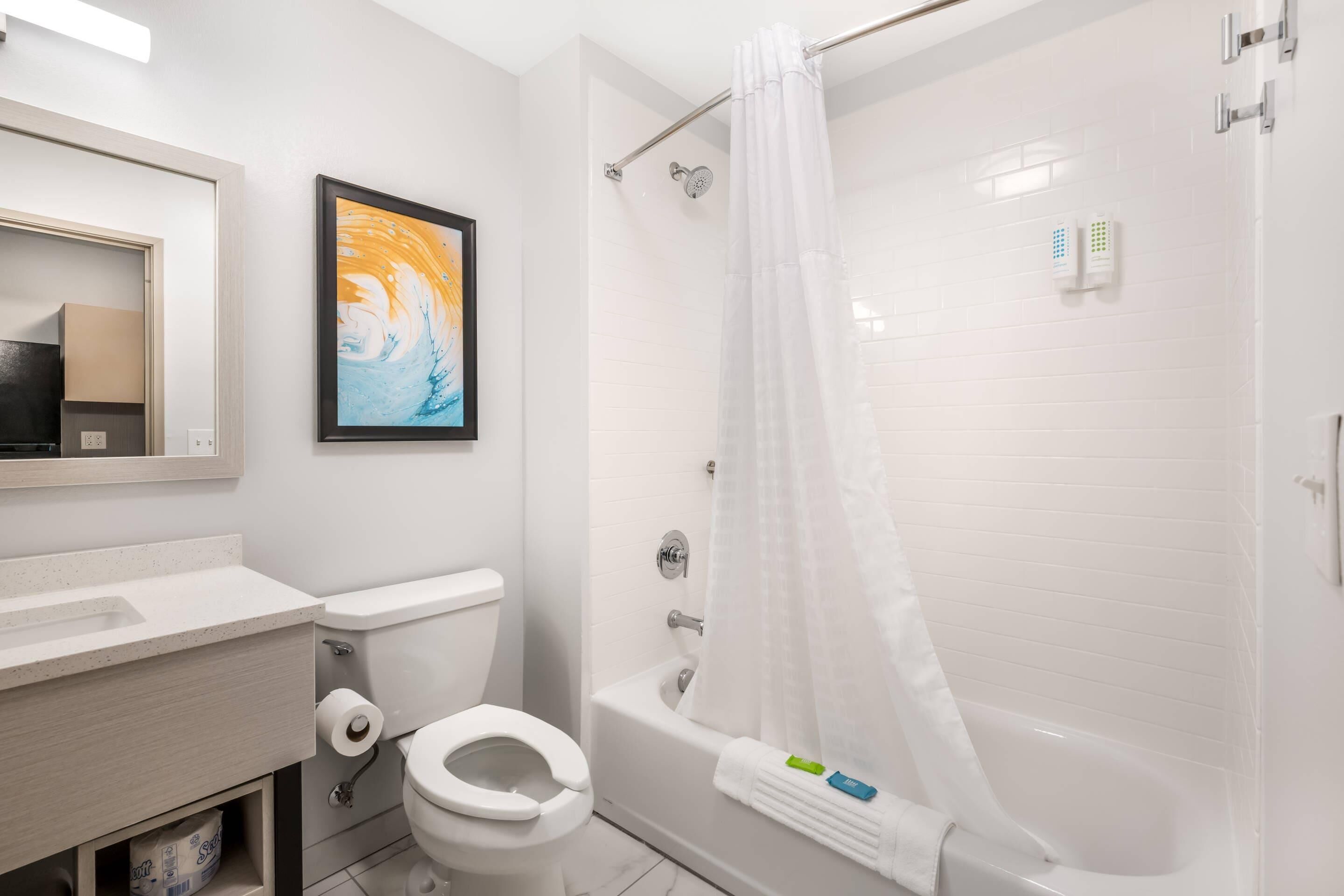 A bathroom with a toilet, sink, shower, and a framed picture on the wall.