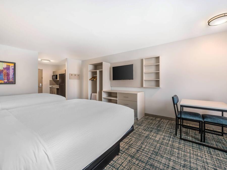 A hotel room with a large bed, a desk with a chair, a TV, and a wardrobe.