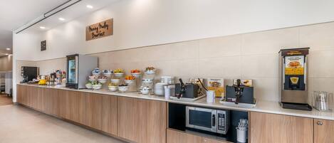 A breakfast bar with a waffle batter dispenser, a microwave, and various food items.