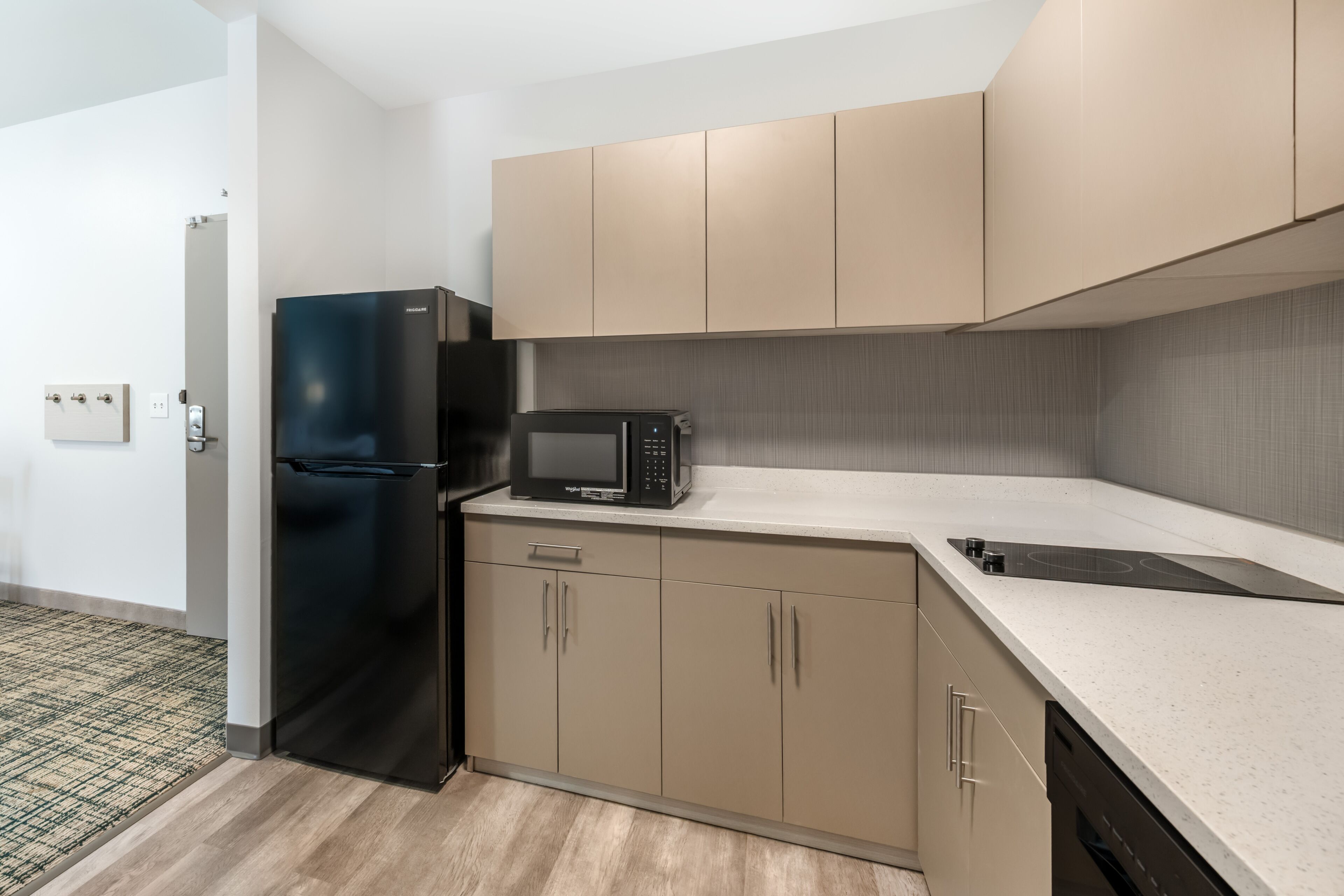 A compact kitchen with a black refrigerator, a microwave, and beige cabinets.