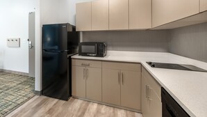 A compact kitchen with a black refrigerator, a microwave, and beige cabinets. - MainStay Suites Harrisburg Airport - Hershey South (Middletown)