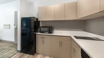 A compact kitchen with a black refrigerator, a microwave, and beige cabinets.