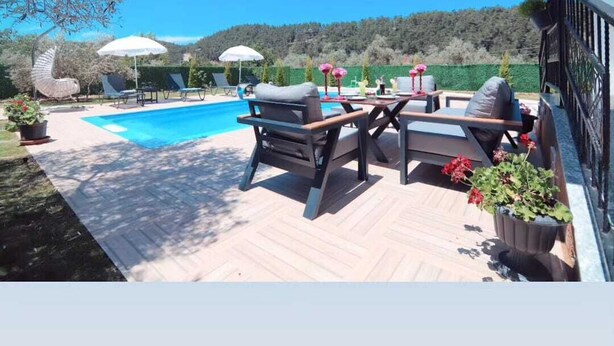 An outdoor pool area with lounge chairs and umbrellas, surrounded by a wooden deck and potted plants.