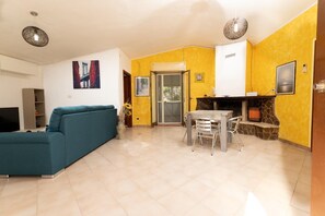 A living room with a teal sofa, a dining table with chairs, a fireplace, and a yellow accent wall.