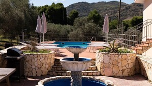 Un área de piscina con una fuente, macetas de piedra, sillas de descanso y una parrilla.