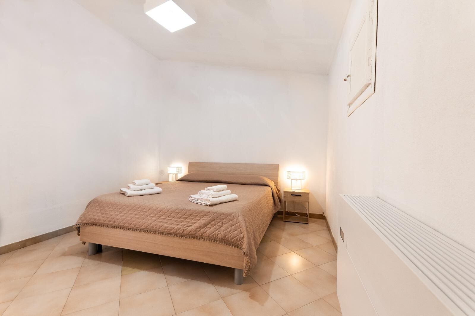 Un dormitorio pequeño y bien iluminado con una cama individual, dos mesitas de noche y un radiador.