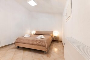 A small, well-lit bedroom with a single bed, two bedside tables, and a radiator.